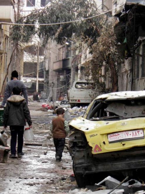 People walk past a damaged car along a damaged street in the besieged area of Homs. REUTERS/Thaer...