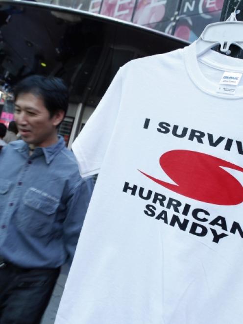 People walk past a "I Survived Hurricane Sandy" t-shirt hanging on a rack for sale in Times...