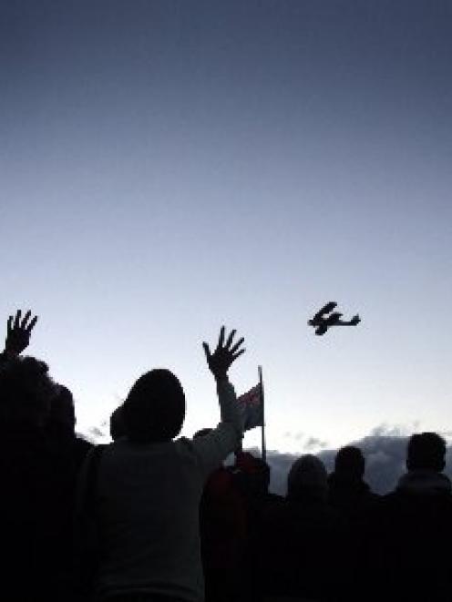 People wave to a Tiger Moth pilot during a flyover at the Lake Hawea Anzac Day dawn service in...