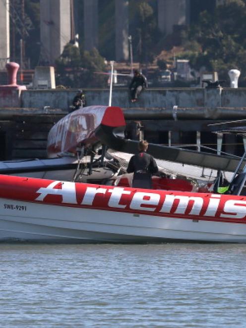 Personnel on a team boat survey damage to the Artemis Racing AC-72 catamaran as it sits in the...