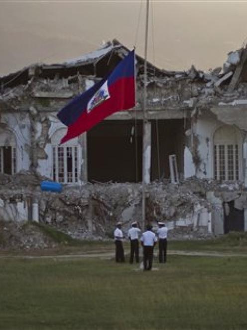Police lower the national flag in front of the damaged presidential palace on the first...