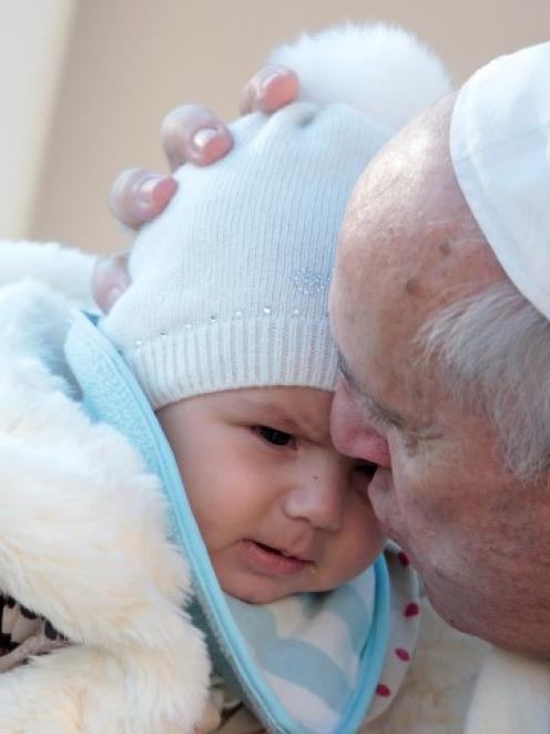 Pope Francis kisses a baby as he arrives to lead his Wednesday general audience in Saint Peter's...