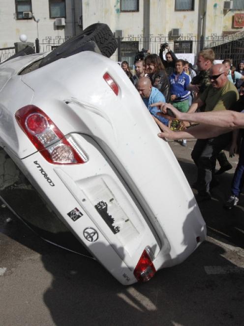 Pro-Ukrainian people overturn a car during a rally in front of the Russian embassy in Kiev. Photo...