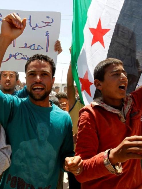 Refugees hold Syrian opposition flags and shout slogans against Syria's President Bashar al-Assad...