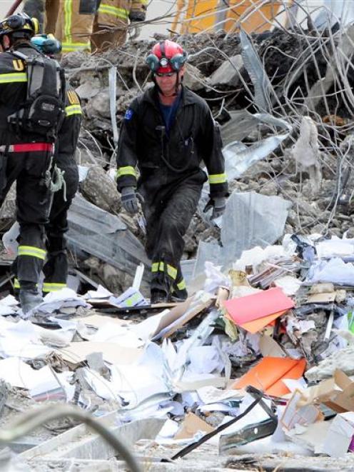 Rescue personnel walk through paper and office items in the remains of the CTV building in...