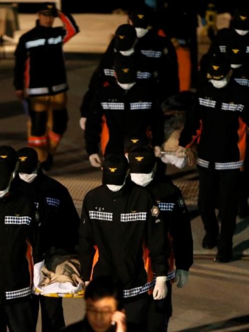 Rescue workers carry the bodies of passengers from the capsized ferry, at a port where family...