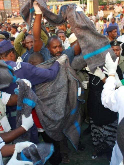 Rescuers assist survivors from a ferry sinking at the port of Zanzibar. At least 24 people are...