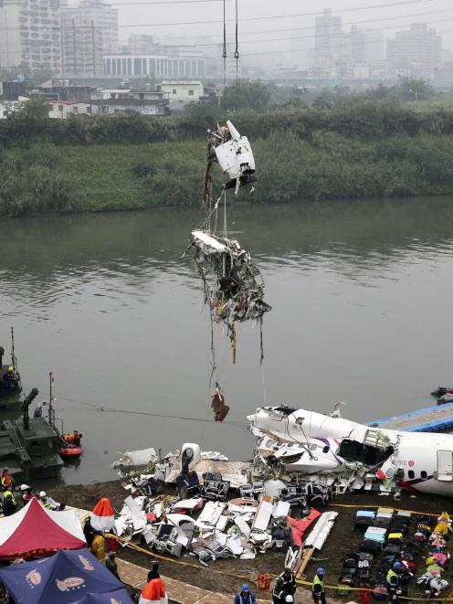 Rescuers lift part of the wreckage of TransAsia Airways plane Flight GE235 after it crash landed...