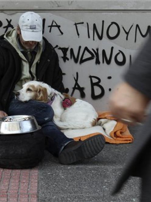 Roberto, an English-Italian man who lives in Greece with his dog, begs as the sign behind him...