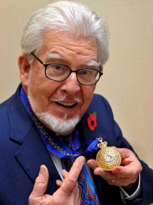 Rolf Harris holds the Officer of the Order of Australia award, which was presented to him by High...