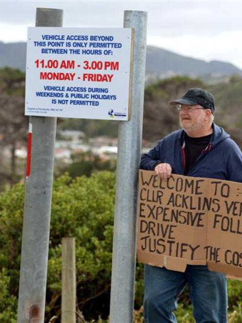 Roy Robertson holds a placard denouncing the Dunedin City Council's decision to reopen the road.