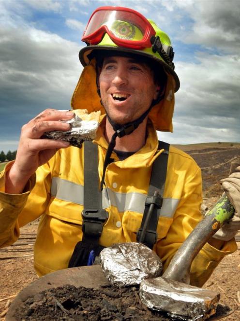 Rural firefighter Will McBeth, of Glenorchy, eats a pie heated by smouldering remains of the...
