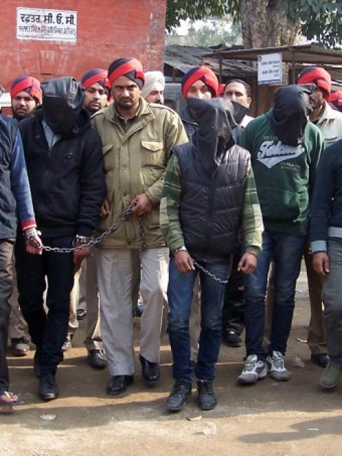 Six men (faces covered) accused of a gang rape in Punjab are escorted by police to a court at...