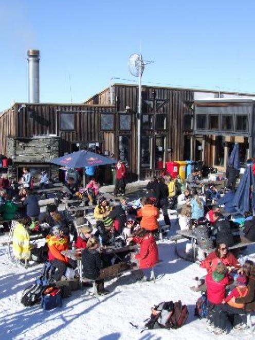 Skiers and snowboarders take a break on the sun deck at Treble Cone skifield. Photo by Matthew...