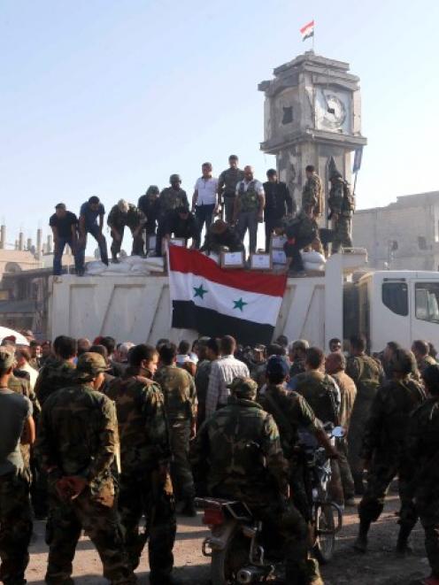 Soldiers loyal to the Syrian regime and civilians gather as they place the Syrian national flag...
