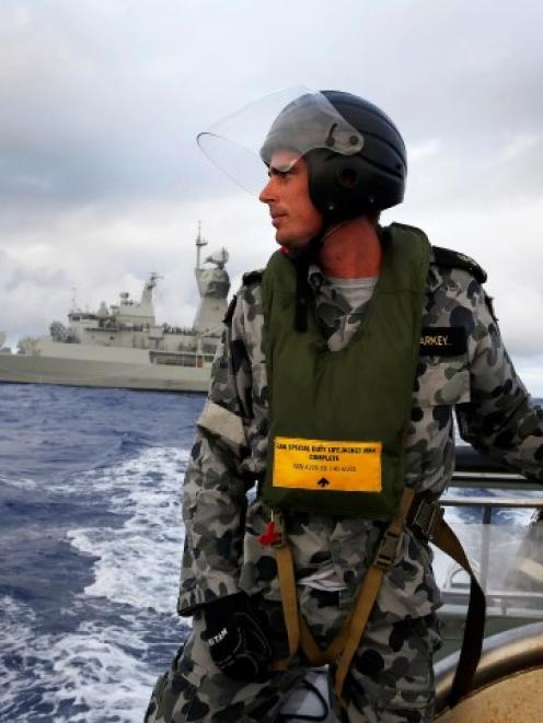 Standing in a rigid hull inflatable boat launched from the Australian Navy ship HMAS Perth,...