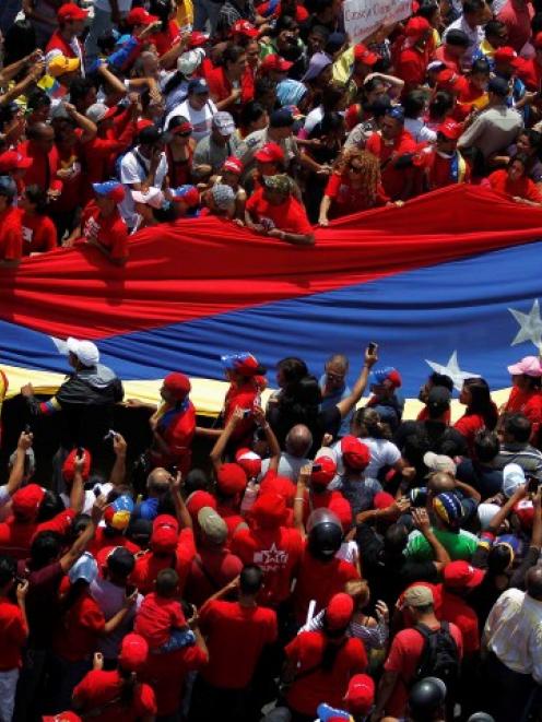 Supporters of Venezuela's late President Hugo Chavez unfurl a large national flag as they gather...