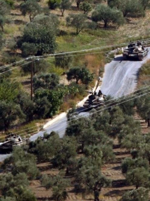 Syrian tanks, seen from the Turkish village of Saribuk, drive towards the town of Darkush in...