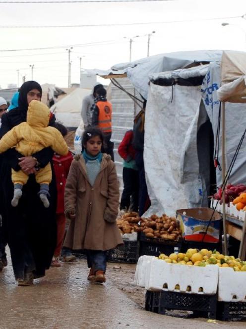 Syrians refugees walk near street vendors after heavy rain, at the Al-Zaatari refugee camp in the...