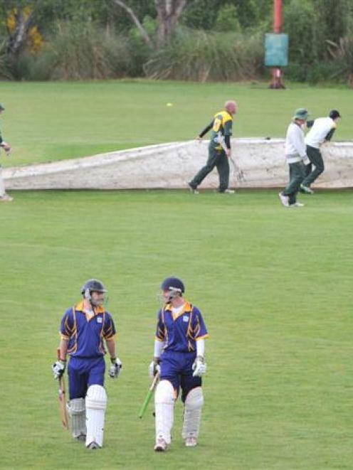 Taieri batsmen Ash Simpson (left) and Toby Batchelor walk off the field as the covers go on at...