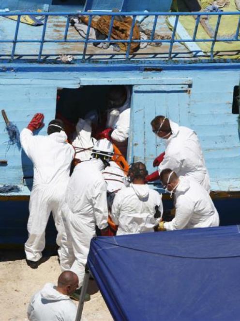 The body of a migrant is carried off a fishing boat, on which 19 migrants died last month.  The...