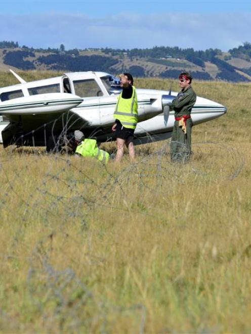 The pilot and the female passenger stand by as aircraft engineers inspect  damage to a 1969 Piper...