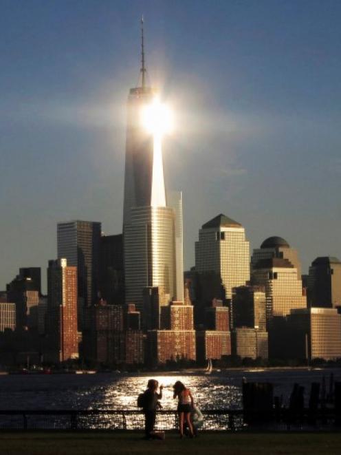The sun reflects off New York's One World Trade Center as people stand in a park in Hoboken, New...