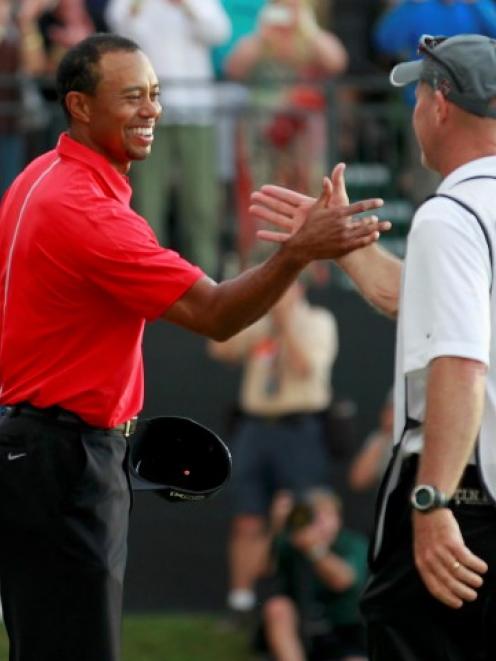 Tiger Woods celebrates with his caddie Joe LaCava after sinking his final putt on the 18th green...