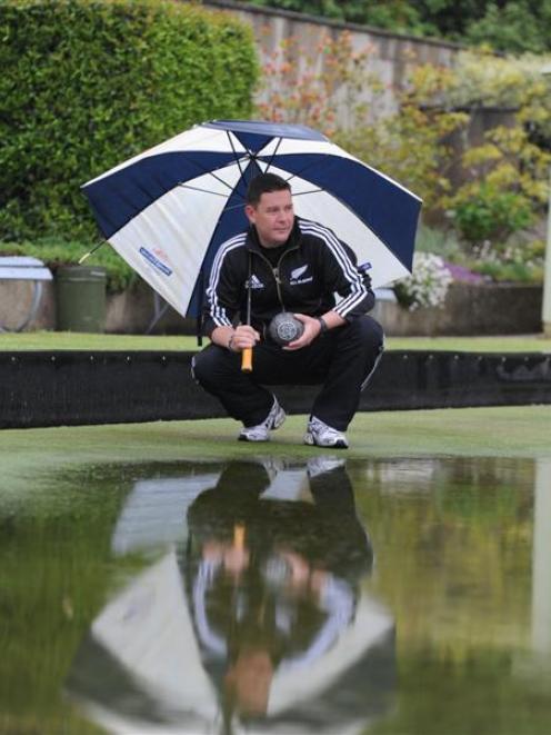 Tony Grantham inspects the rain-soaked greens at the North East Valley club yesterday. Play in...