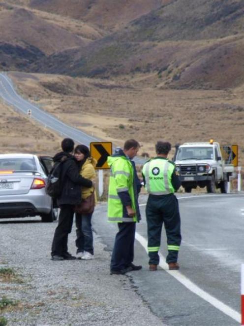 Two Chinese tourists watch at an accident scene in the Lindis Pass on Thursday, where a car in...