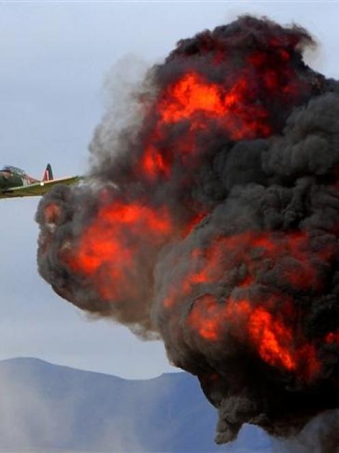 A Harvard flies past a fireball from a mock airfield attack at Warbirds over Wanaka. Photo by...