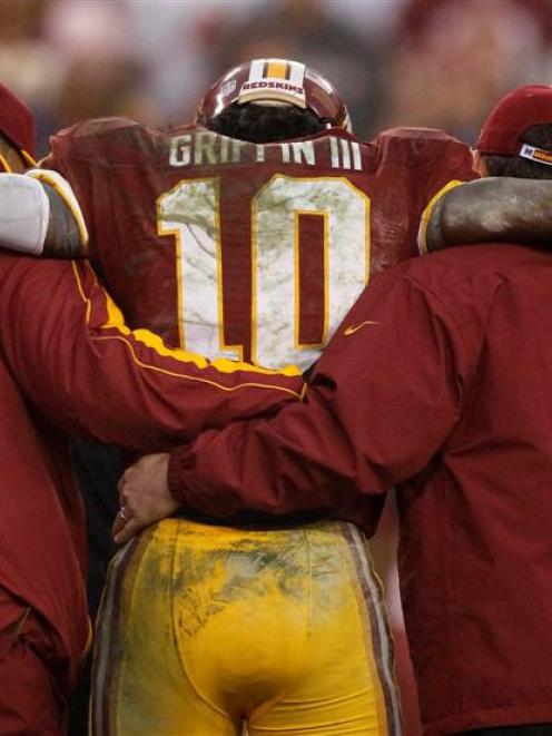 Washington Redskins starting quarterback Robert Griffin III is helped off the field by team...