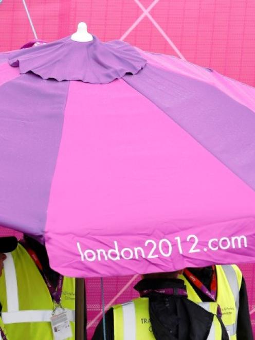 Workers shelter from rain under a parasol in the London 2012 Olympic Park at Stratford in London...