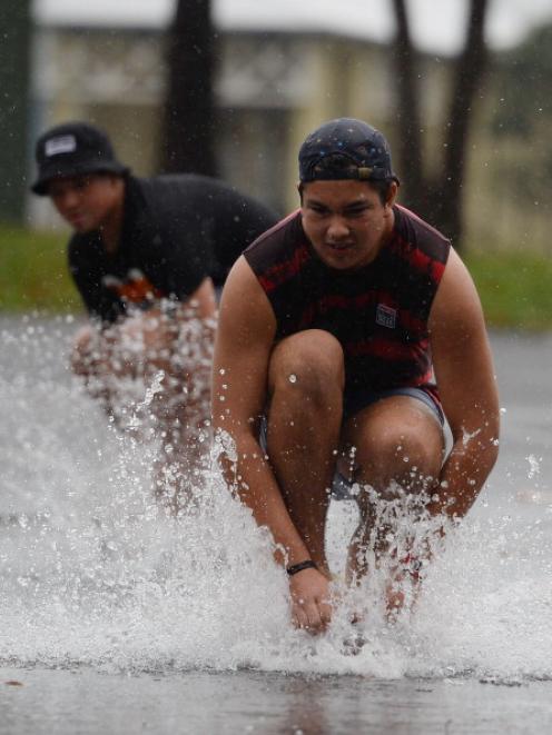 Young men ride skateboards through pools of water formed by heavy rain before Cyclone Ita makes...
