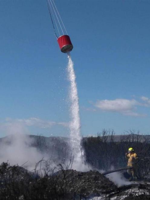 A helicopter helps a firefighter douse the Waitaki River island fire in January. PHOTO: SUPPLIED