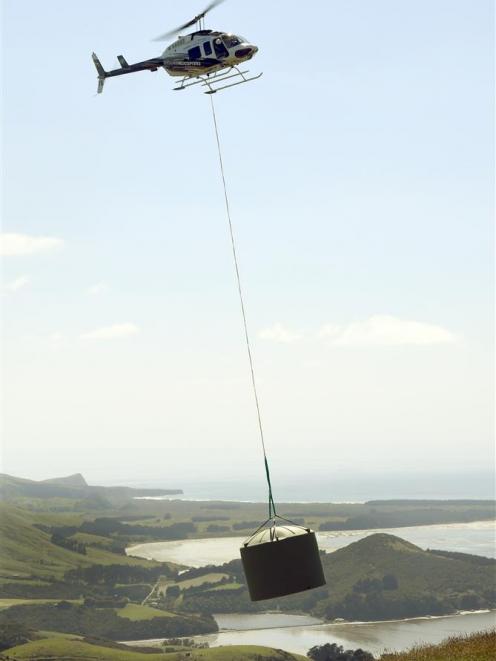 Pilot Paul Williams, of Highland Helicopters, lifts one of two 26,000-litre water tanks that will...