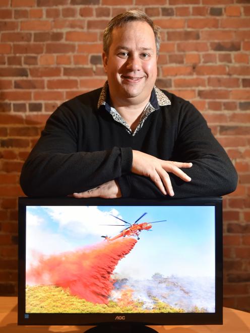 TracPlus Global chief executive Trevor McIntyre with a photo of an Erickson aircrane dropping retardant on a fire in South Australia. Photo: Gregor Richardson