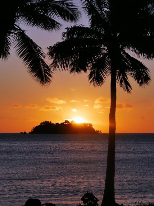The sun sets behind the small island directly in front of a beachside bure at Tropica Island...