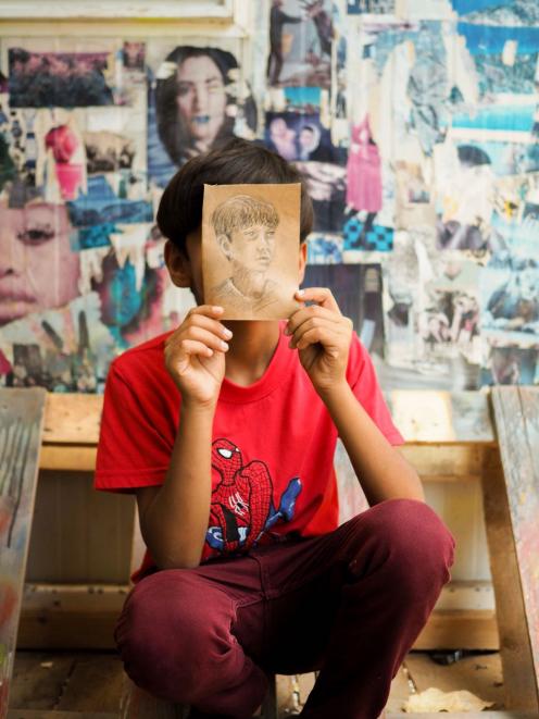 A young refugee at the Ritsona camp holds up a picture of himself, drawn by Mr Olsen. 
...