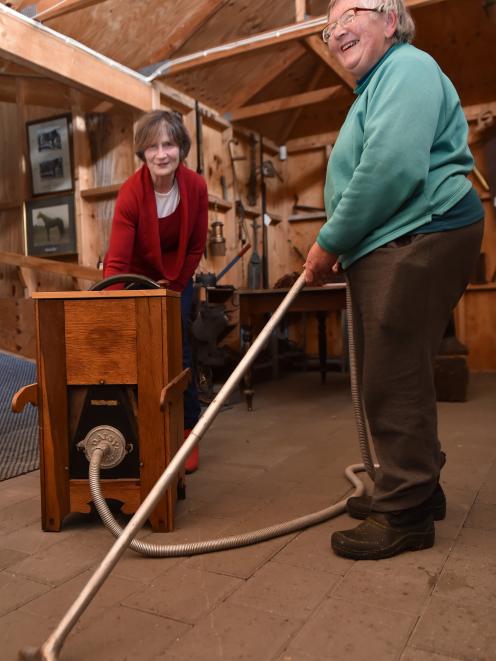 Juliet Jones turns the handle while Irene Ramsay holds the hose of an early 20th century vacuum cleaner.