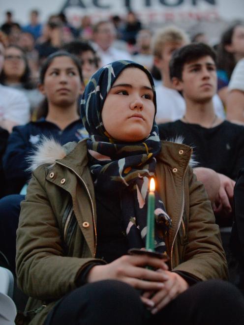 A woman holds a candle in the crowd during last night's civic vigil at Forsyth Barr Stadium in...