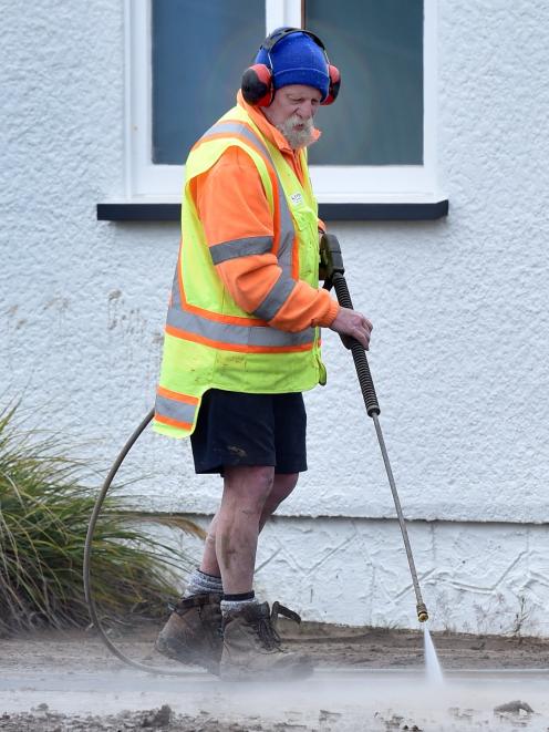 A contractor water blasts the footpath after flooding in Macandrew Bay on Tuesday.
