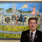 Prof John Broughton, CNZM, stands in front of a painting by Ivan Hill depicting the professor and...