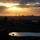 A man washes himself in a small pond as the sun sets over a village on the outskirts of...