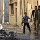 A boy carries a weapon as he walks with members of the Free Syrian Army on a damaged street...