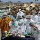 A Buddhist monk and residents pray in front of a makeshift incense stand in Namie, northeastern...