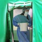 A medical doctor wearing proper protective gear carries a container inside a tent meant for...