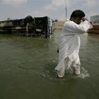 A Pakistani man passes by a toppled passenger bus along a flooded street in Muzaffargarh, Punjab...