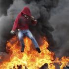 A Palestinian protester jumps over burning tyres during clashes with Israeli troops near the...