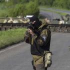 A Ukrainian soldier, with armoured personnel carriers behind him, points his weapon at an...